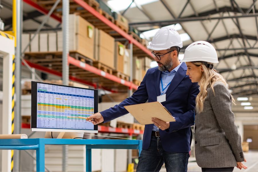 Two supply chain managers examine predictive analytics data on a computer in a warehouse
