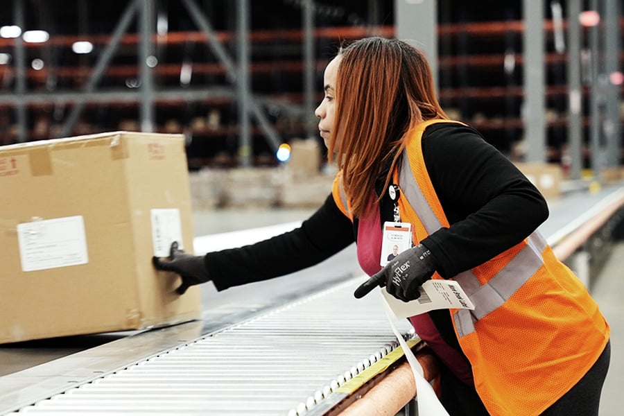 Ryder warehouse worker in a safety vest lifting a box in a distribution center Ryder warehouse worker in a safety vest lifting a box in a distribution center