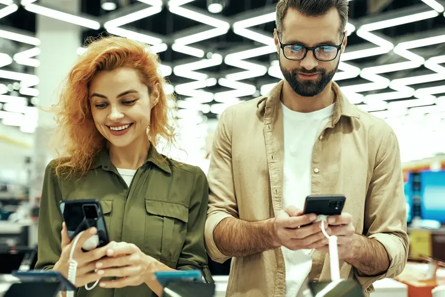 Two shoppers comparing products on their smartphones in a consumer electronics store
