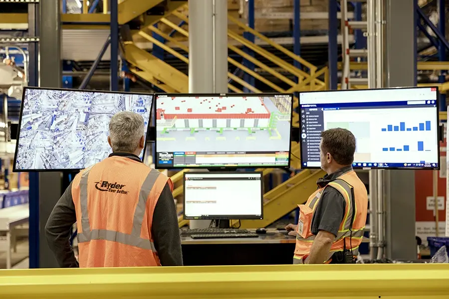 Ryder warehouse team in safety vests monitoring inventory data on screens in a distribution center TESTRyder warehouse team in safety vests monitoring inventory data on screens in a distribution center