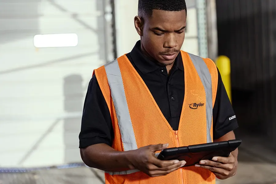 Ryder worker in a safety vest reviewing construction schedules on a tablet at a job site Ryder worker in a safety vest reviewing construction schedules on a tablet at a job site