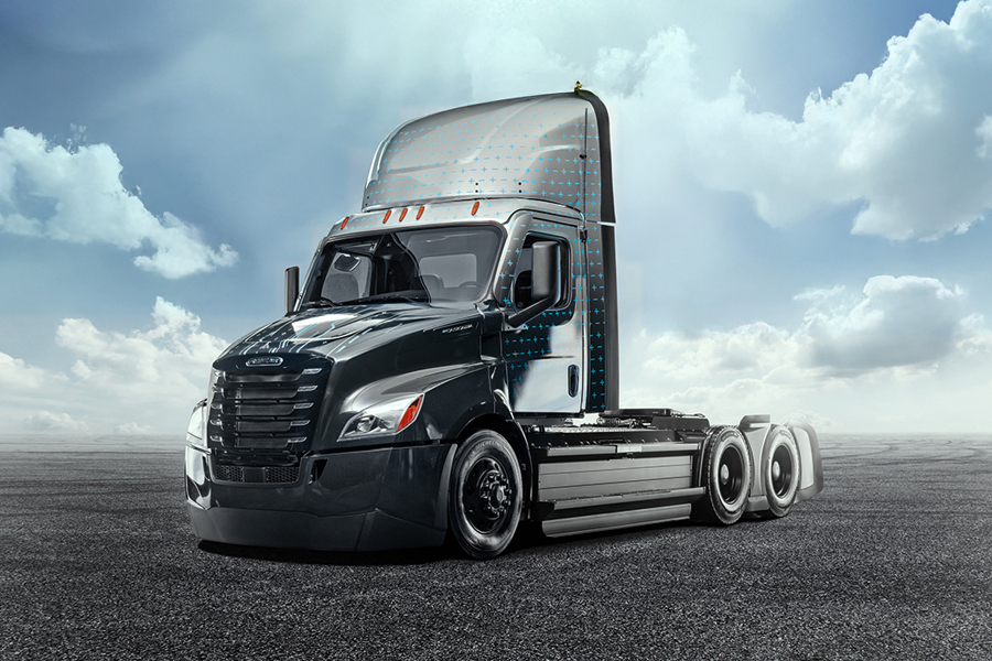 Black electric semi day cab tractor parked on pavement under a cloudy sky